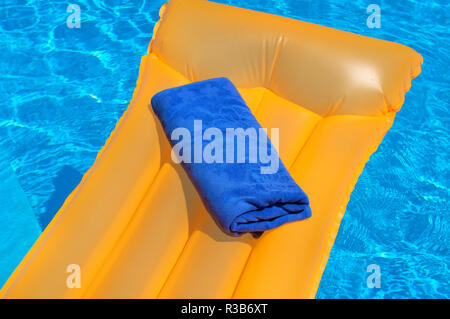 Blau Handtuch auf eine Orange aufblasbare Matratze Schwimmen im Pool Stockfoto