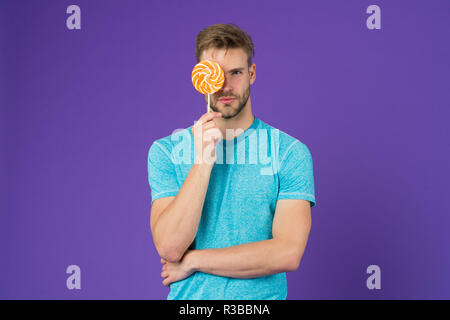 Mann mit Borsten mag Lollipop. Cheat meal Konzept. Zucker schädlich für die Gesundheit. Kerl halten Lollipop candy violett unterlegt. Geschmack der Kindheit. Lollipop Spaß. Mann essen großen bunten süßen Lutscher. Stockfoto