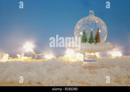 Bild von Weihnachtsbäumen in Glas Kugel über verschneite Holztisch Stockfoto