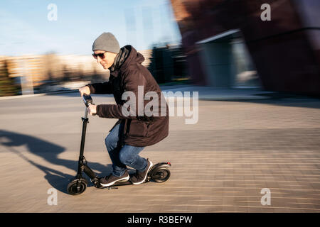 Junger Mann in Freizeitkleidung auf elektrische kick Scooter auf Stadt Straße in motion blur im Herbst Stockfoto