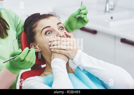 Verängstigten Mädchen an Zahnarzt bedeckt Mund mit den Händen. Konzept Phobie Zahnarztpraxis Stockfoto