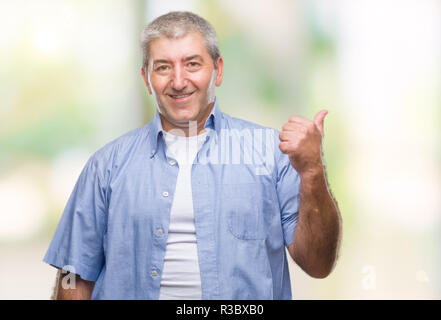 Gut aussehender älterer Mann über isolierte Hintergrund lächelnd mit glücklichen Gesicht und zeigt auf die Seite mit dem Daumen nach oben. Stockfoto