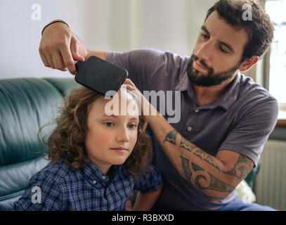 Vater kämmen langes lockiges Haar seines jungen Sohnes zu Hause. Stockfoto