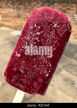 Frostigen eis Textur auf ein rotes Eis am Stiel mit einem industriellen Hintergrund der Bürgersteig und Ziegeln. Stockfoto