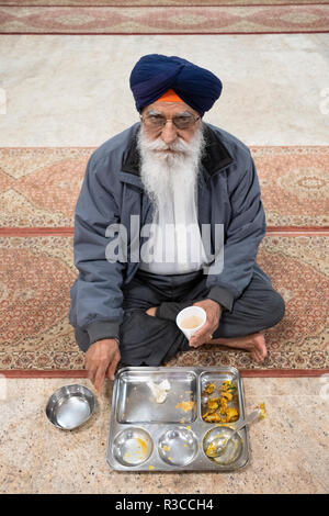 Eine ältere Sikh Mann mit einem weißen Bart und Turban essen eine kostenlose Mahlzeit in einem langar in einem Sikh-tempel in Queens, New York. Stockfoto