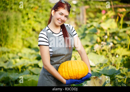 Portrait von glücklichen Mädchen mit Kürbis in die Hände am Garten im Sommer Tag. Defokussiertem Hintergrund. Stockfoto