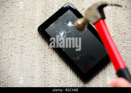 Hämmern Bildschirm des Tablet durch alte rostige Hammer auf konkreten Hintergrund Stockfoto