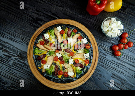 Hot aromatisiert köstliche italienische Pizza auf schwarz Teig mit Fleisch, Gemüse und Käse auf einem dunklen Holz- Board. Stockfoto