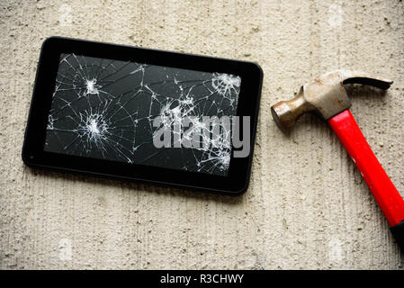 Gebrochene tablet Bildschirm mit rotem rostige Hammer in der Nähe von Es auf konkreten Hintergrund Stockfoto