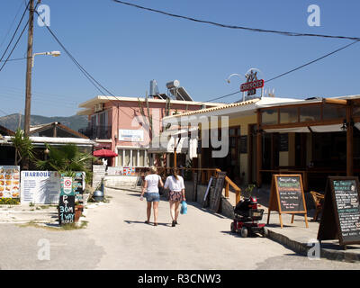 Touristen zu Fuß entlang der Beach Road in Roda, Korfu, Griechenland zwischen Crusoes Pub und den Hafen Bar Stockfoto