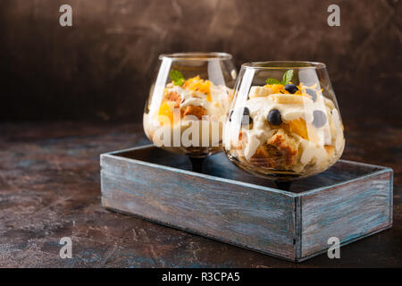 Zwei Gläser mit Gesunden hausgemachte layered Dessert trifle mit Orange, Heidelbeere, Keksen, Joghurt und Müsli Stockfoto