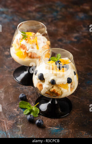 Zwei Gläser mit Gesunden hausgemachte layered Dessert trifle mit Orange, Heidelbeere, Keksen, Joghurt und Müsli Stockfoto
