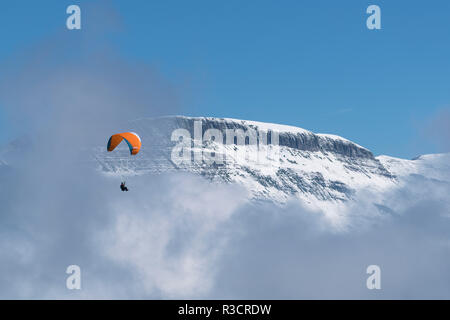 Eine parasailer schwebt über den Wolken durch die schneebedeckten Gipfel im Berner Oberland Region der Alpen, in der Nähe von Grindelwald, Schweiz. Stockfoto