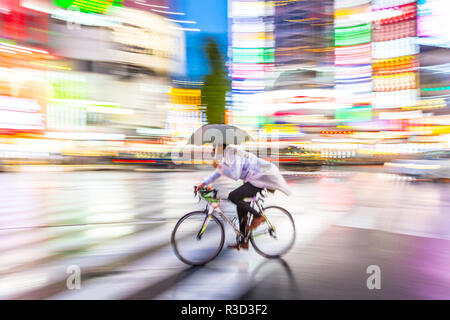 Tokio, Japan - eine lokale Fahrrad Holding einen Regenschirm mit den Lichtern der Stadt im Hintergrund bluried Stockfoto