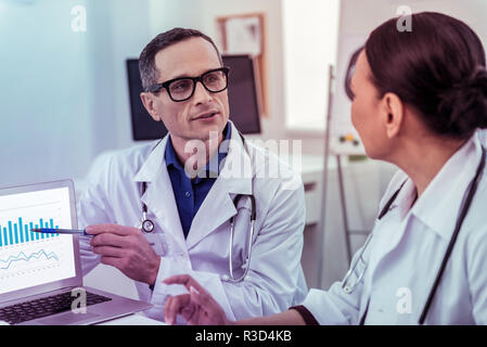 So ernst. Hübscher junger Mann mit Brille und zeigen auf dem Bildschirm des Laptops Stockfoto