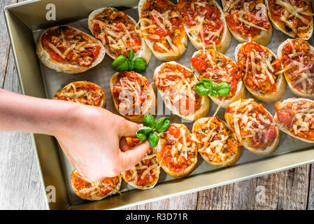 Koch Zubereitung italienisches Essen - garnieren Bruschetta mit gerösteten Tomaten, Basilikum und Käse, kochen Hausgemachte Vorspeisen für die Partei Stockfoto