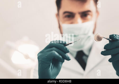 Professionelle Werkzeuge. Selektiver Fokus der medizinischen zahnmedizinische Instrumente in den Händen der qualifizierten Zahnarzt bei einem Blick auf ihre Mundhöhle Stockfoto