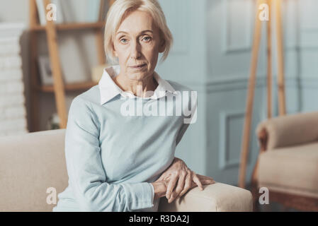 Nachdenkliche Stimmung. Ernsthafte gealterte Frau auf dem Sofa sitzen, während Sie auf der Suche Stockfoto