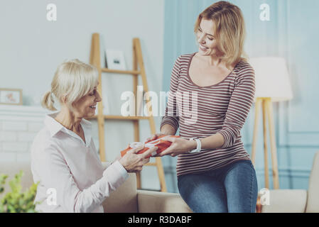 Angenehme Überraschung. Liebevolle ältere Mutter, die ein Geschenk von ihren Jungen schöne Tochter und es während der schönen Zeit bei hom Stockfoto
