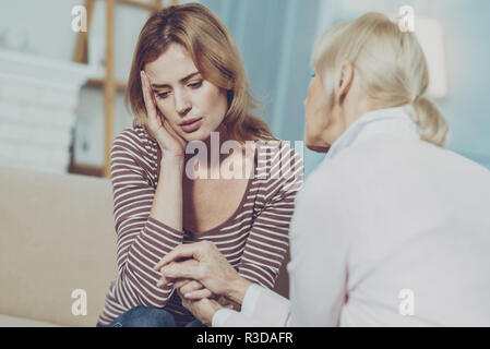 Mütter lieben. Liebevolle ältere Mutter umarmte ihre traurige junge Tochter und trösteten, während ihre Hände halten und eng sitzen Stockfoto