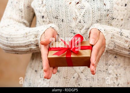 Frau mit einem Geschenk Box mit einem roten Band in die Hände gebunden. Flache Tiefenschärfe, selektiver Fokus auf der Box. Konzept für ein Geschenk im Urlaub Stockfoto