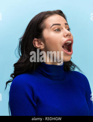 Das überrascht und erstaunt junge Frau schreiend mit offenen Mund auf blauem Hintergrund isoliert. Konzept der Schock angesichts der menschlichen Emotion Stockfoto