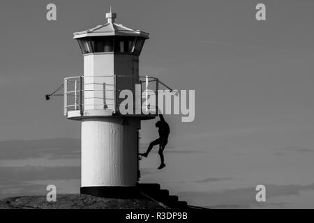 Die Silhouette eines jungen Menschen hängen von einem Leuchtturm mit einer Hand in Schwarz in Weiß Stockfoto