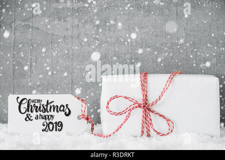 Etikett mit englischen Kalligraphie frohe Weihnachten und einen guten Rutsch ins Jahr 2019. Eine weiße Geschenk mit roter Ribbn. Grunge Zement Hintergrund mit Schnee und Schneeflocken Stockfoto