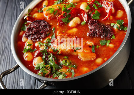 Close-up von herzhaften Fabada Asturiana Bohneneintopf mit Chorizo, Speck und Blut Wurst in eine Kasserolle aus Metall auf einem schwarzen Holztisch, spanische Küche, Ho Stockfoto