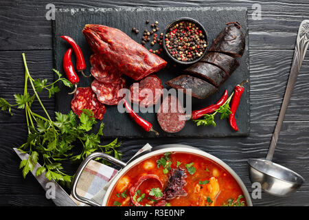 Close-up Fabada Asturiana Bean herzhaften Eintopf. wichtigsten Zutaten - in Scheiben Chorizo, Blut würstchen Pfeffer und Petersilie auf einem Schneidebrett, Spanisch c Stockfoto