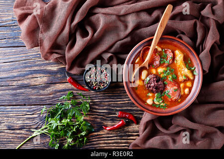 Die Fabada Asturiana Bean Würstchen herzhaften Eintopf in einem Steingut Schale mit Löffel auf einem rustikalen Holztisch mit braunem Stoff, spanische Küche, Blick von Abo Stockfoto