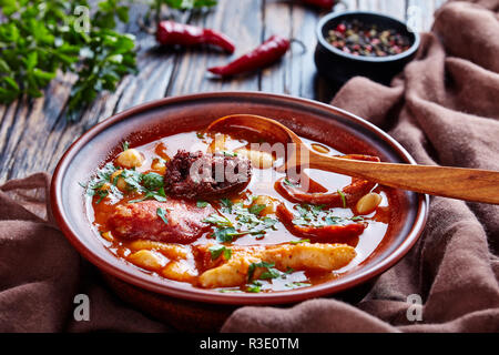 Die Fabada Asturiana Bean herzhaften Eintopf in einem Steingut Schale mit Löffel auf einem rustikalen Holztisch mit braunem Stoff, spanische Küche, Ansicht von oben Stockfoto