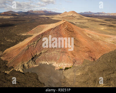 Luftaufnahme der Bermeja Berg von einer intensiv roten Farbe, von lavafeldern umgeben. Lanzarote, Kanarische Inseln, Spanien Stockfoto