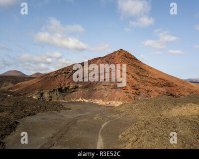 Luftaufnahme der Bermeja Berg von einer intensiv roten Farbe, von lavafeldern umgeben. Lanzarote, Kanarische Inseln, Spanien Stockfoto