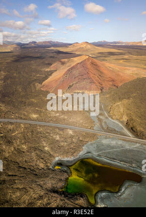 Luftaufnahme der Bermeja Berg von einer intensiv roten Farbe, von lavafeldern umgeben. Küstenstraße fließt durch einen kleinen See. Stockfoto