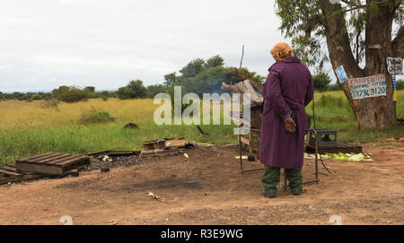 Arme afrikanische Frau arbeitet und am Straßenrand Grillen stehen oder braaing Mais oder miellies auf einer temporären Grill in Südafrika Stockfoto