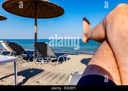 Man Beine bis zum Sonnenbaden ist liegend sorglos in Liege neben der Küste, am öffentlichen Strand. Stockfoto