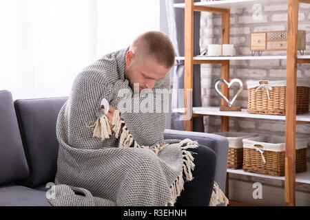 Kranke junge Frau mit Decke auf dem Sofa sitzen Stockfoto