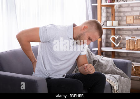 Junge Mann sitzt auf einem Sofa mit Rückenbeschwerden Stockfoto