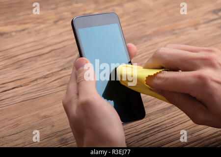 Mann Reinigung Mobiltelefon mit gelben Tuch über Holz- Schreibtisch Stockfoto