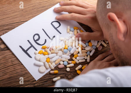 Man's Hand, die Pillen mit Hilfe Text auf Papier über Holz- Schreibtisch Stockfoto