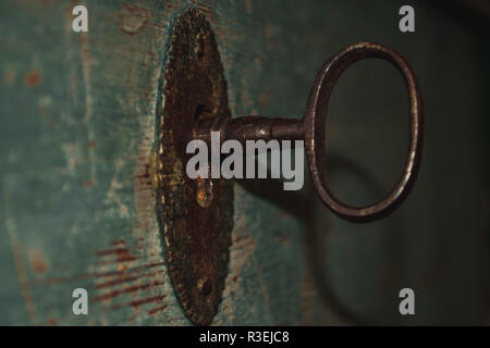 Ein alter rostiger Schlüssel in einem Schlüsselloch einer türkisfarbenen Holztür Stockfoto