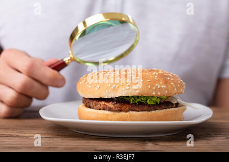 Des Menschen Hand mit Lupe mit frischen Burger Stockfoto