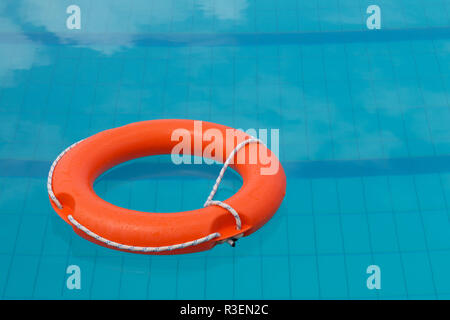 Helles orange Schwimmweste Schwimmen im Sommer Tag auf der Oberfläche des blauen Wasser im Pool. Orange leben Boje. Wasserrettung Notfallausrüstung. Stockfoto