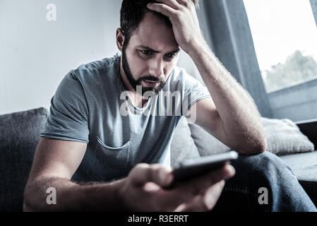 Tief in Gedanken versunken. Aufmerksame bärtige männliche Faltenbildung Stirn berühren und Kopf beim Lesen der Nachricht Stockfoto