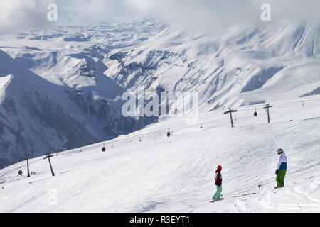 Zwei Snowboarder steigen auf verschneiten Skipiste und Gondelbahn bei Sun bewölkten Tag. Georgien, Region Gudauri. Kaukasus Berge im Winter. Stockfoto