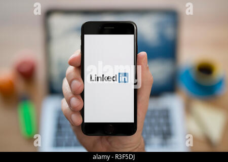 Ein Mann schaut auf seinem iPhone die zeigt die LinkedIn logo, während saß an seinem Computer Schreibtisch (nur redaktionelle Nutzung). Stockfoto