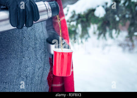 Man gießt heißen Tee aus der Thermoskanne im Winter Wald Stockfoto