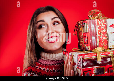 Studio geschossen von einer jungen Frau, die in der isländischen Pullover holding Geschenkboxen auf rotem Hintergrund. Weihnachten oder Silvester feiern. Stockfoto