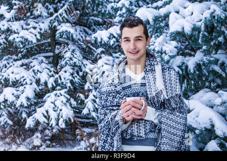 Junge Frau hält Tasse Kaffee mit Marshmallow im Winter Wald Stockfoto